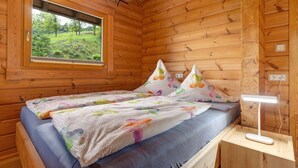 Una habitación de cabaña de madera con una cama, una ventana y una mesita de noche con una lámpara.