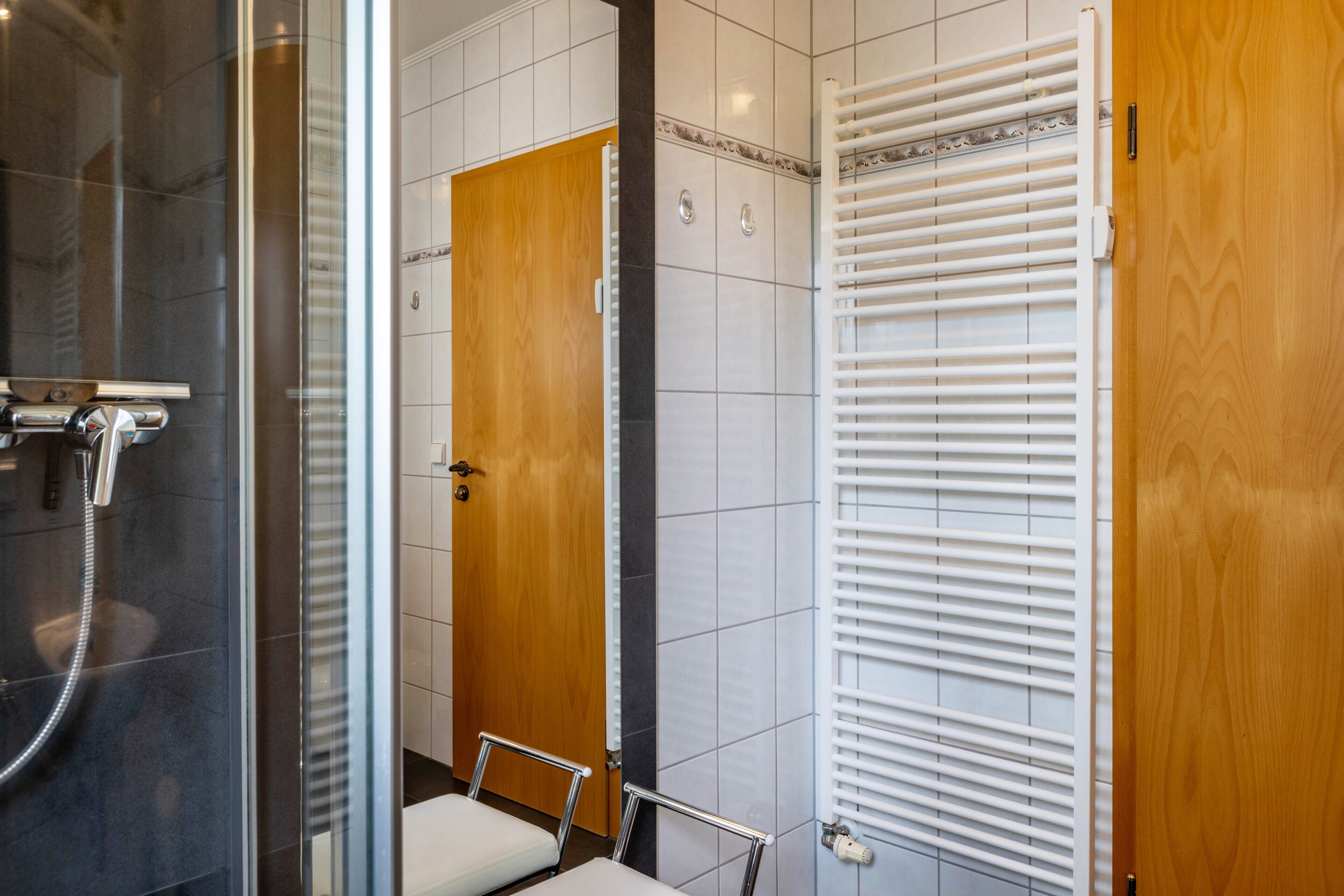 Een badkamer met een glazen douchecabine, een houten deur en een betegelde muur.