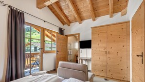 Een slaapkamer met een bed, een stoel, een houten garderobe en een televisie.
