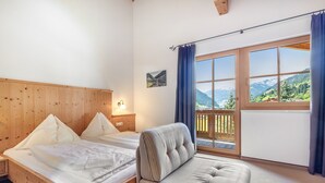 Een kamer met een houten bed, een bank, een raam met uitzicht op bergen en een schilderij aan de muur.
