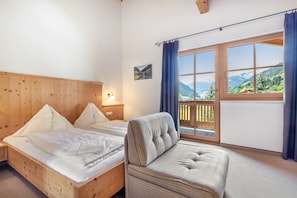 Una habitación con una cama de madera, un sofá, una ventana con vistas a montañas y un cuadro en la pared.