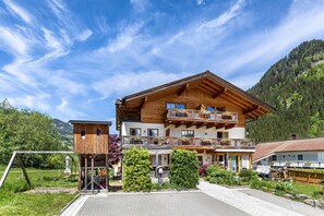 Een meerlaags houten gebouw met balkons, een skilift en een bergachtig landschap op de achtergrond.
