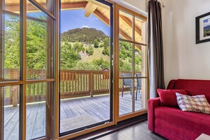 A room with a red sofa, large windows with a view of a deck and forested hills. - Apartment 'Stockinger' with Mountain View, Shared Garden and Wi-Fi (Grossarl)