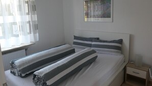 Un dormitori amb dos llits, una tauleta de nit, un quadre al mur i cortines transparents a la finestra.