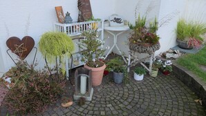 Un pati pavimentat amb plantes en testos, una tanca blanca i una decoració rústica amb forma de cor metàl·lic.