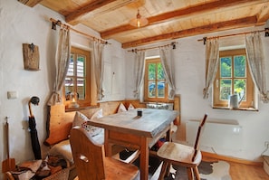 Une pièce rustique en bois, avec une grande table, des chaises, un banc et une fenêtre avec des rideaux.