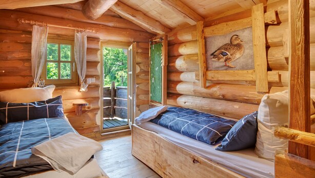 Un dormitori de cabana de fusta amb un llit, una banca i una finestra.
