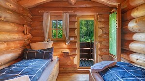 Un dormitori de cabana de fusta amb dos llits, una taula petita i una finestra amb cortines.