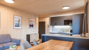 Cocina moderna con microondas, lavamanos y encimera. Hay una mesa de comedor de madera y un sofá gris.