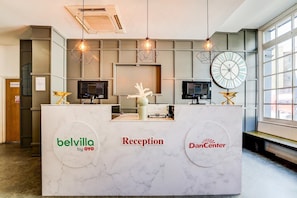 A reception desk with a marble top, two monitors, a clock, and a sign for 'belvilla by OYO'.