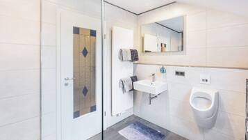 Et moderne badeværelse med en glasbrusekabine, en hvid vask, en pissoir og et spejl over vasken.