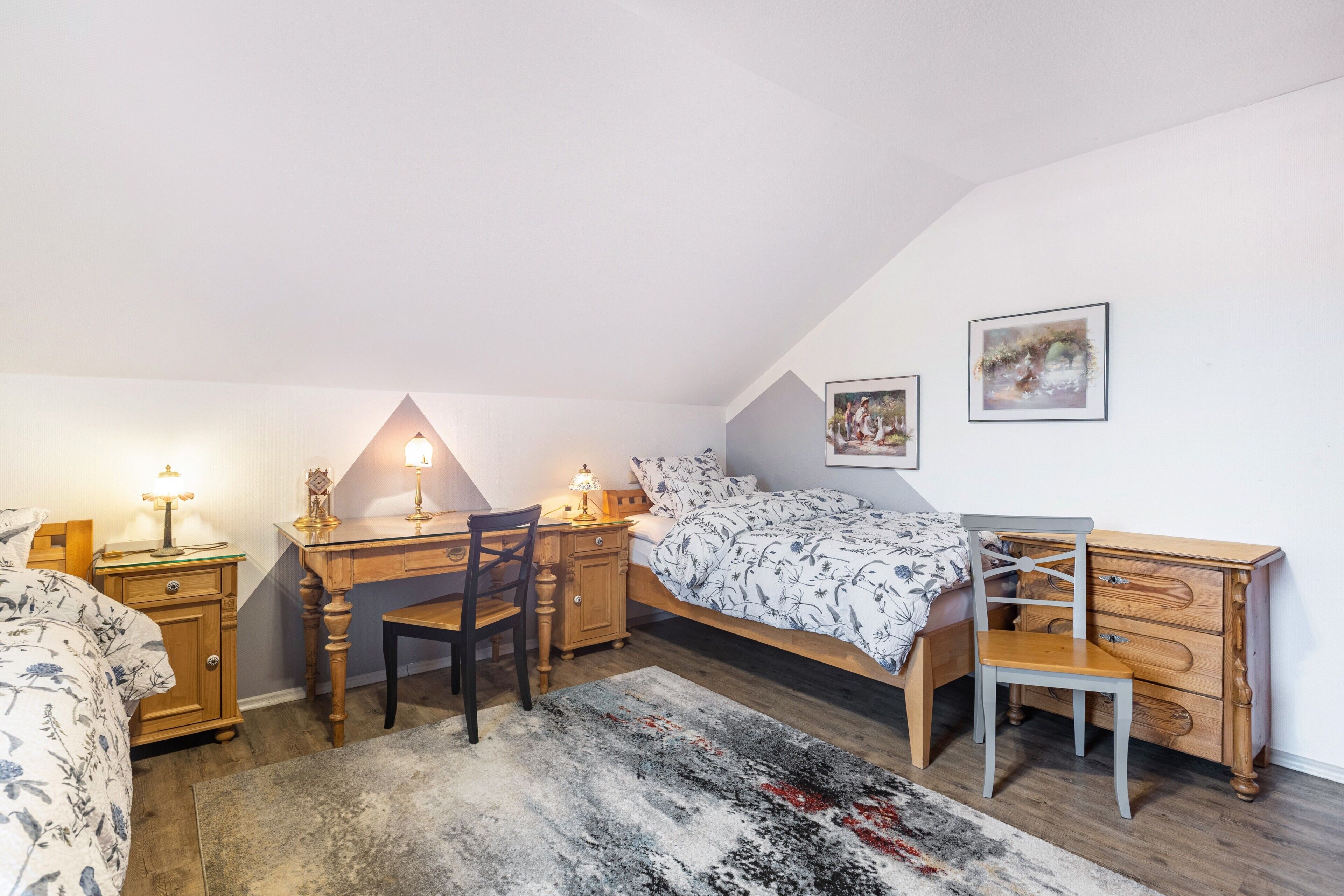 Ein Schlafzimmer mit Bett, Schreibtisch, Stuhl, Kommode und zwei gerahmten Bildern an der Wand.