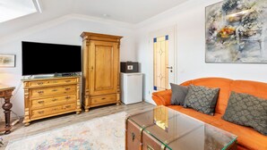 A living room with a television, wooden cabinet, glass coffee table, orange sofa, and a painting on the wall. - Farmhouse 'Zur Henne' with Shared Terrace and Wi-Fi (Weinbach)