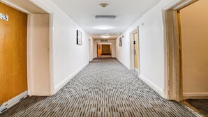 A hotel hallway with a carpeted floor, white walls, and doors on both sides.