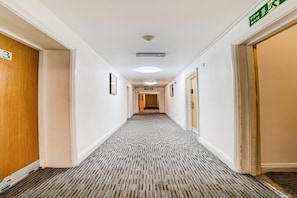 Un pasillo de hotel con piso alfombrado, paredes blancas y puertas a ambos lados.