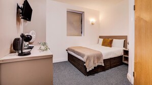 A compact bedroom with a bed, bedside table, and a small window.
