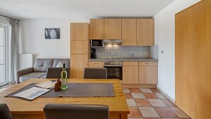 A compact kitchen with wooden cabinets, a microwave, stove, and a dining area with a table and chairs. - Apartment 'Haus 4' with Lake View, Shared Terrace and Wi-Fi (Meersburg)
