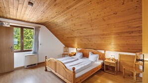 A bedroom with a wooden ceiling, a bed, a nightstand, a chair, and a window with curtains.
