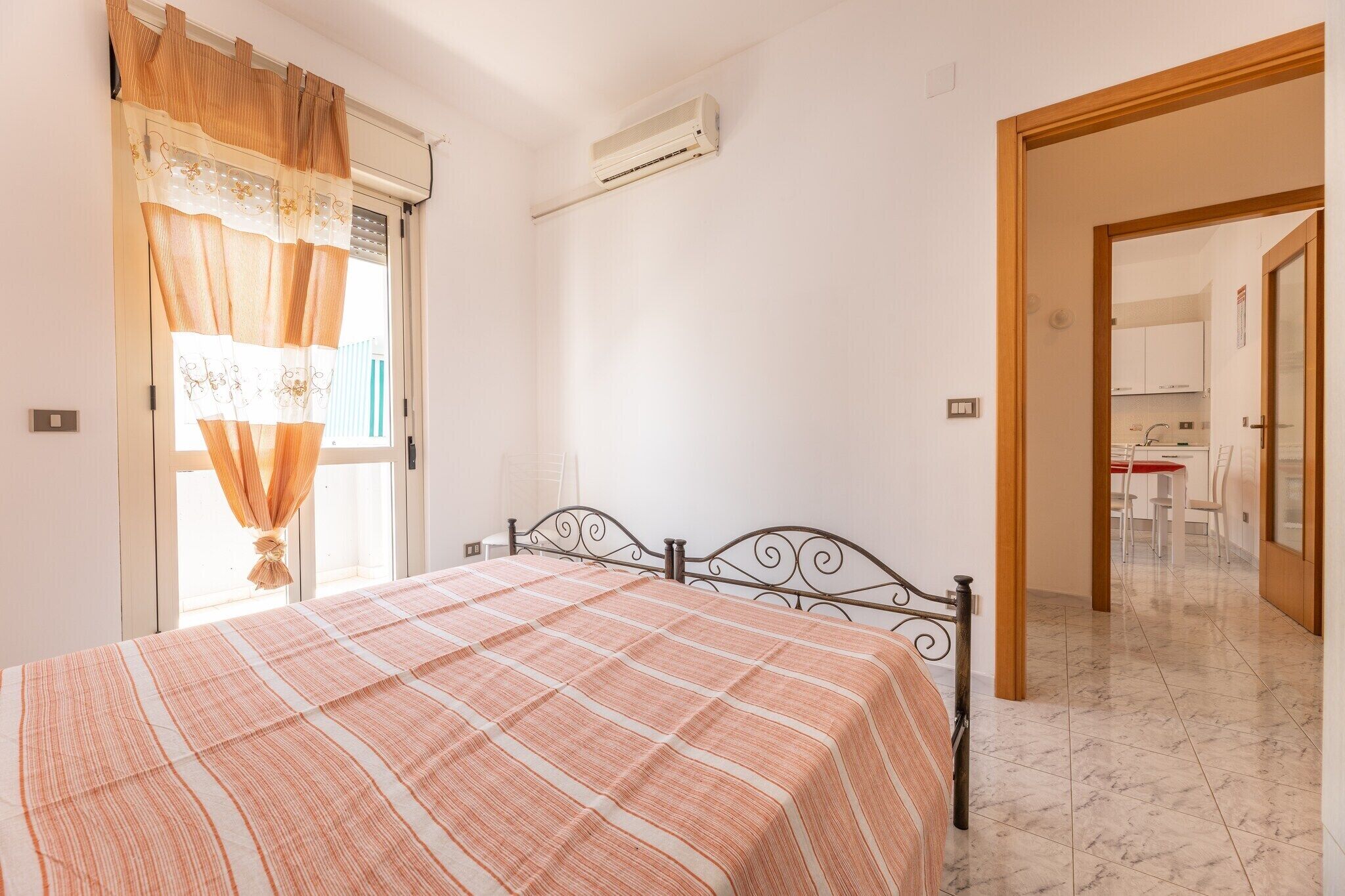 Un dormitorio con cama, aire acondicionado y vista a la cocina por una puerta abierta.