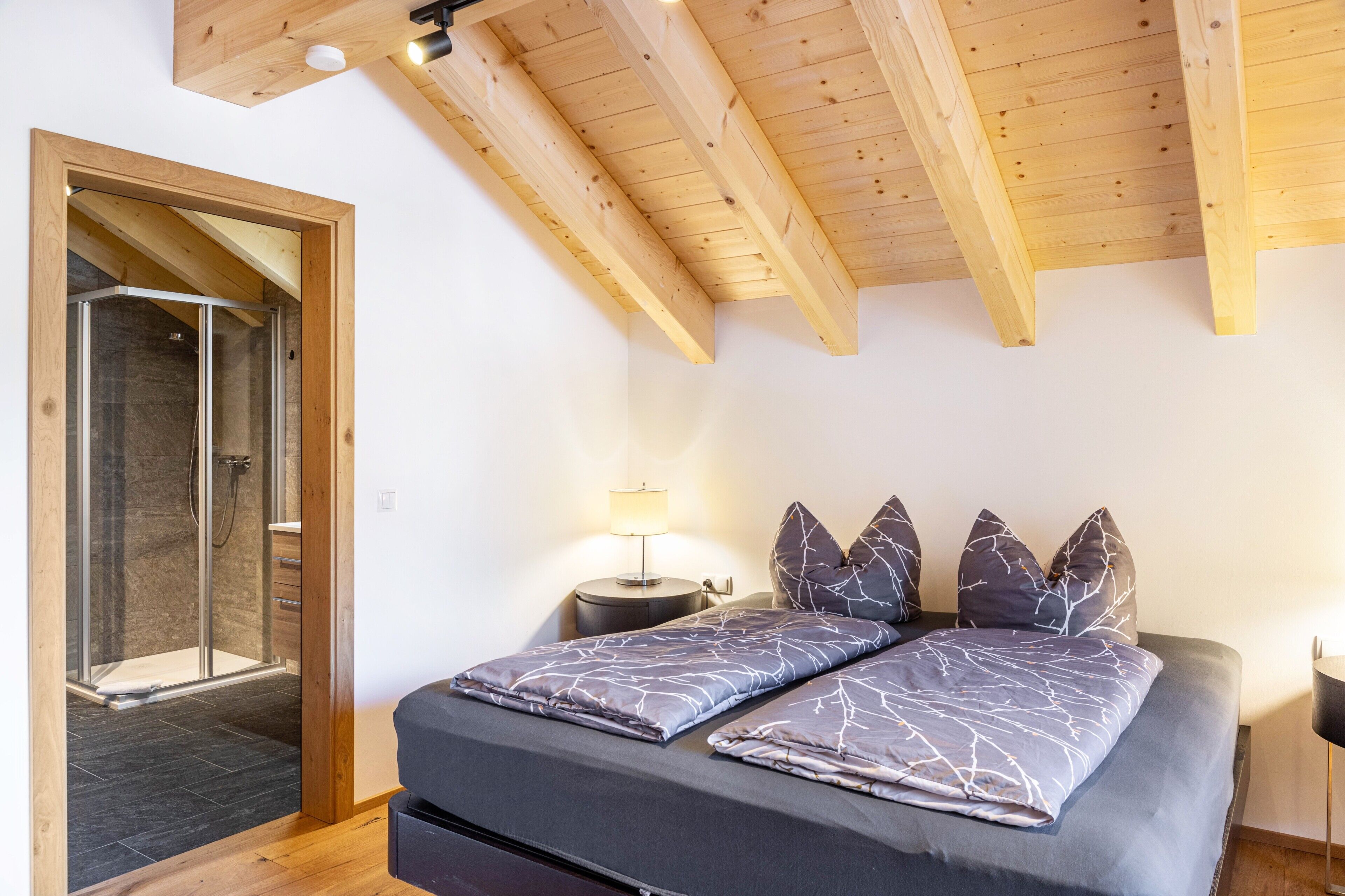 A bedroom with a bed, a nightstand, a lamp, and a wooden ceiling.