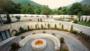 Un área ajardinada con un diseño circular de ladrillos, una fuente central y un parque infantil al fondo.