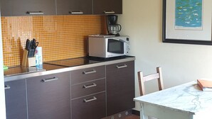 Une cuisine de taille réduite, avec des meubles de couleur sombre, un pare-feu en carrelage, un four à micro-ondes et un tableau encadré au mur.