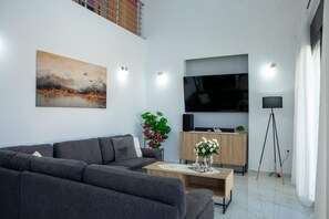 Un soggiorno moderno con un divano grigio, un televisore a schermo piatto, un mobile in legno, una lampada da terra e un quadro appeso al muro.