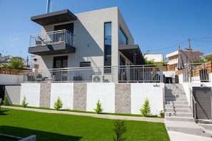 A modern two-story building with a balcony, a staircase, and a well-maintained lawn.