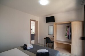 A bedroom with a bed, a desk, a chair, a wardrobe, and a television on the wall.