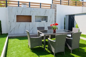 Una terrazza esterna con un muro in marmo, un camino in mattoni e un tavolo con sedie in vimini.