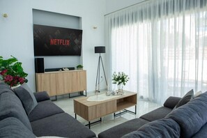 A modern living room with a flat-screen TV, a wooden coffee table, and grey sofas.
