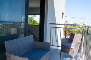 A balcony with wicker furniture, a glass door leading to an indoor area, and a view of the surrounding buildings.