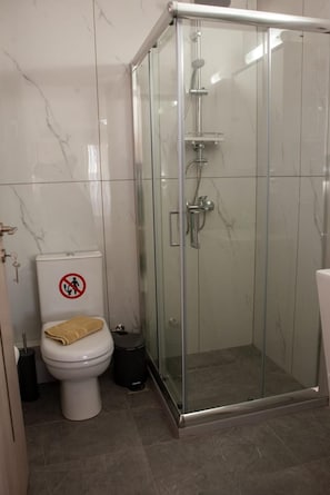 Un bagno moderno con doccia vetro, un WC con cartello di divieto di pausa e un asciugamano sul coperchio.