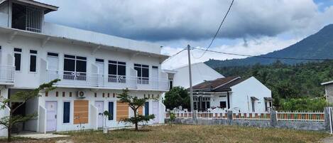 A two-story white building with balconies, a small attached structure, and a mountain in the background.
