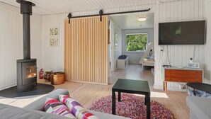 A modern living room with a wood-burning stove, a sofa with colorful cushions, a television, and a sliding door leading to another room.