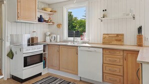 A kitchen with white cabinets, a stove, a dishwasher, and a window with a view of greenery.
