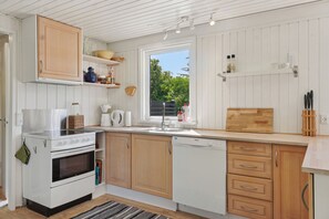 A kitchen with white cabinets, a stove, a dishwasher, and a window with a view of greenery.