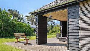 A wooden deck with a bench, a covered outdoor seating area, and a building with a sloped roof.