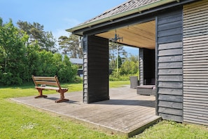 A wooden deck with a bench, a covered outdoor seating area, and a building with a sloped roof.