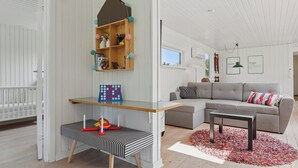 A living room with a white crib, a gray sofa, a wooden shelf with colorful balls, and a striped bench.