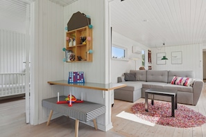 A living room with a white crib, a gray sofa, a wooden shelf with colorful balls, and a striped bench.
