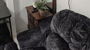 Ein Zimmer mit einem großen Spiegel, einem an der Wand befestigten Fernseher, einer kleinen Holzkommode und einem gemusterten Sofa.