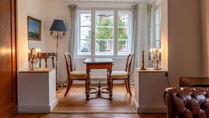 Een eetgedeelte met een houten tafel en stoelen, een kroonluchter en uitzicht door een raam.