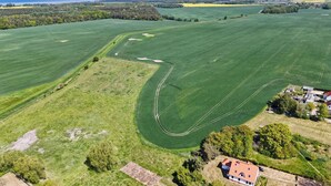 Eine Vogelperspektive eines ländlichen Anwesens mit weitläufigen grünen Feldern, einem gewundenen Weg und einer kleinen Gruppe von Gebäuden mit rotem Dach.