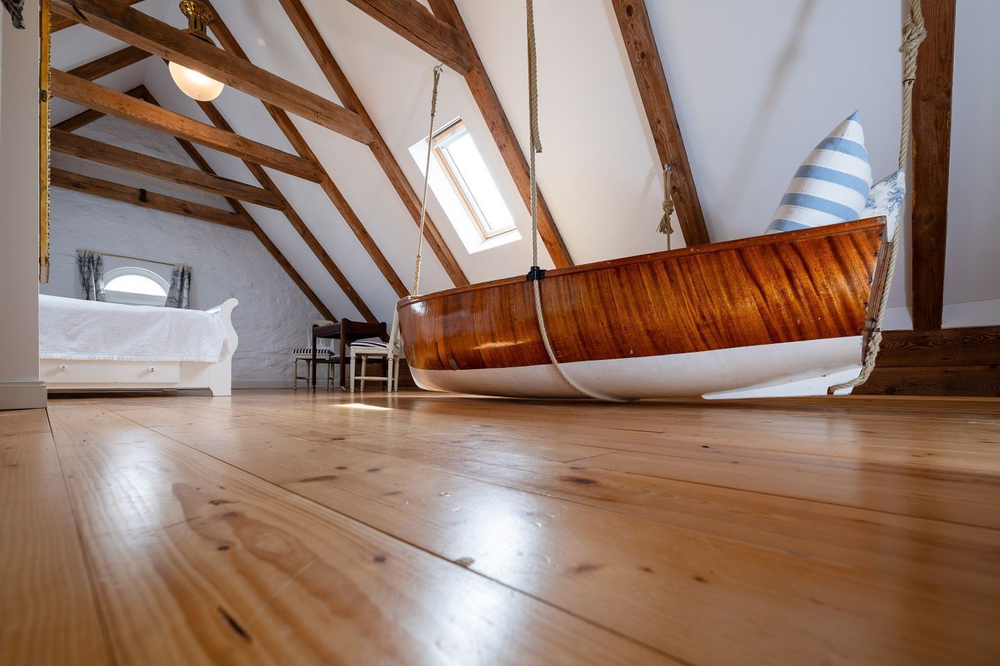 Ein schiffsförmiges Bett in einem Schlafzimmer im Zwischengeschoss mit Holzbalken, einem Oberlicht und Blick zum Himmel.