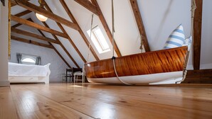 Ein schiffsförmiges Bett in einem Schlafzimmer im Zwischengeschoss mit Holzbalken, einem Oberlicht und Blick zum Himmel.