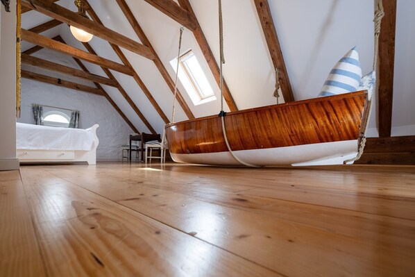A boat-shaped bed in a loft bedroom with wooden beams, a skylight, and a view of the sky.