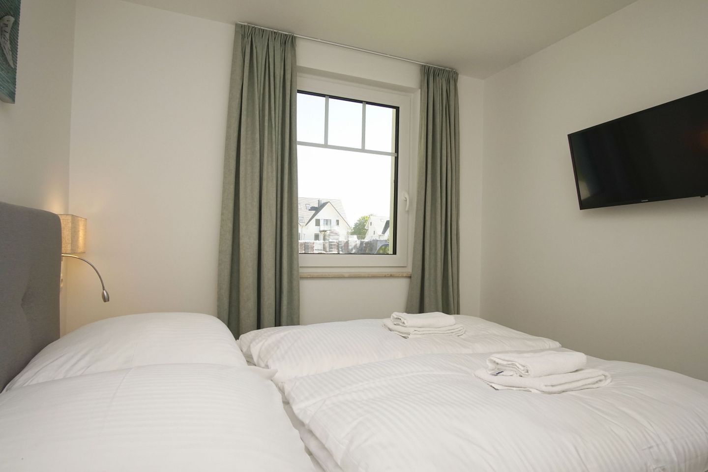 A hotel room with two beds, a window with curtains, a flat-screen TV, and a lamp.