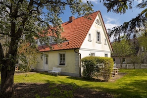 Ein zweistöckiges Haus mit rotem Ziegeldach, weißem Anstrich und einem kleinen Vorgarten mit einer Bank und einer Hecke.