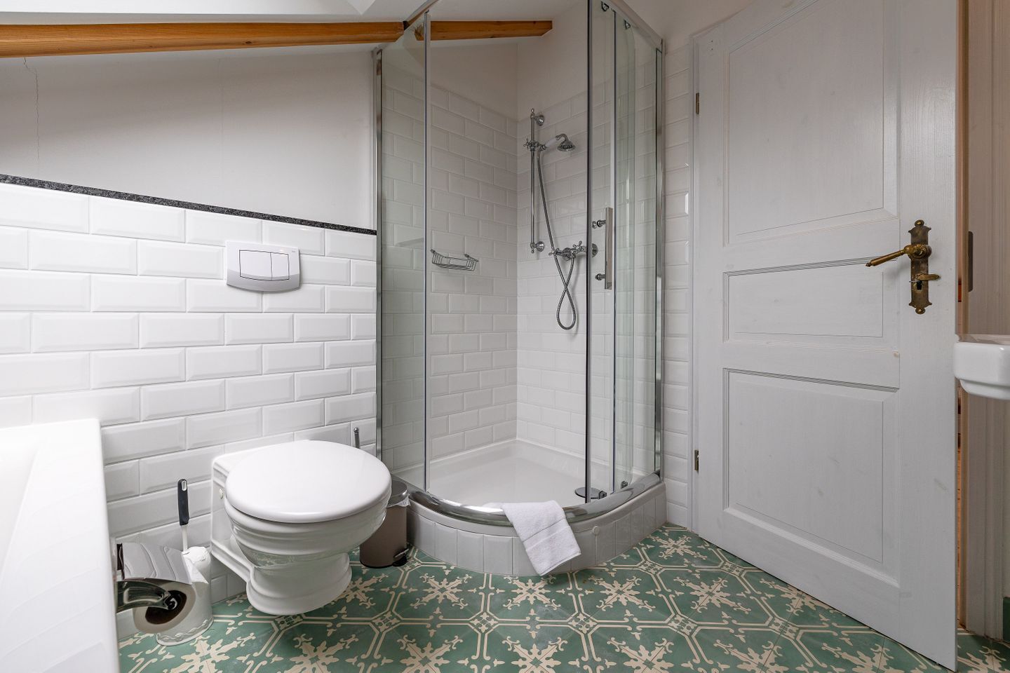 Une salle de bain avec des toilettes blanches, une douche fermée par une paroi de verre et une porte blanche.